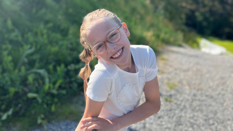 Ung jente med briller smiler og ser i kamera.