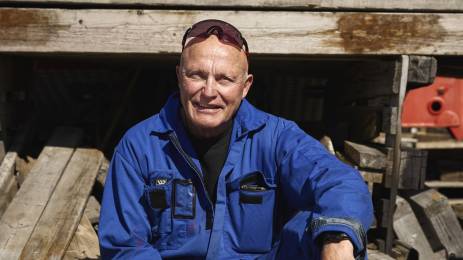 Person i arbeidsklær sitter på en trepall utendørs på en arbeidsplass.