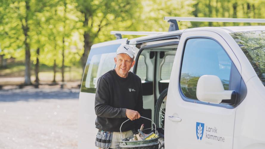 Smilende mann ved en arbeidsbil