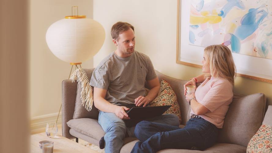 Ung mann med laptop og kvinne med kaffekopp snakker i sofaen