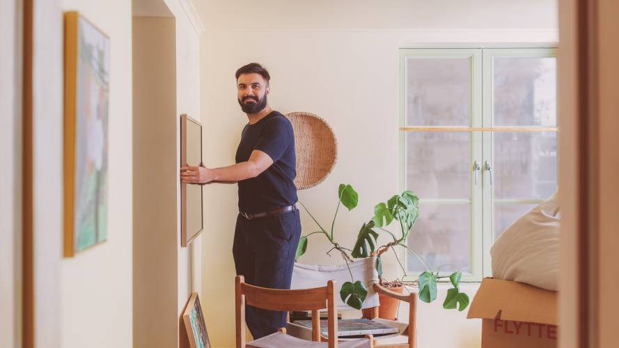 Ung mann ser rett i kameraet og henger opp bilde på stuevegg