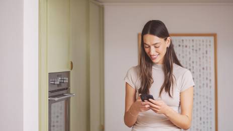 Ung dame med mobil i hendene på kjøkkenet