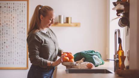 Ung kvinne pakker ut frukt på kjøkkenet