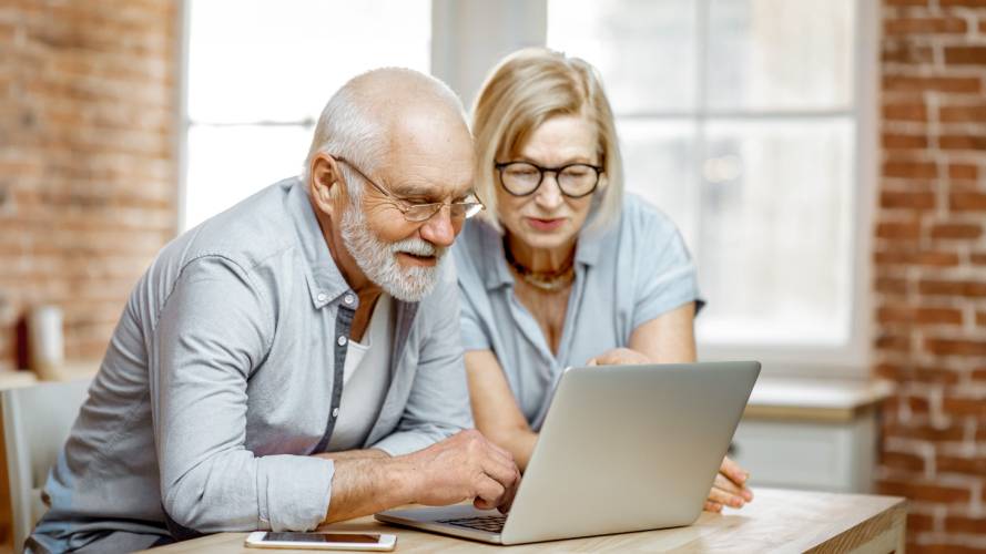 Seniorpar som sitter ved et bord og ser på en laptop 