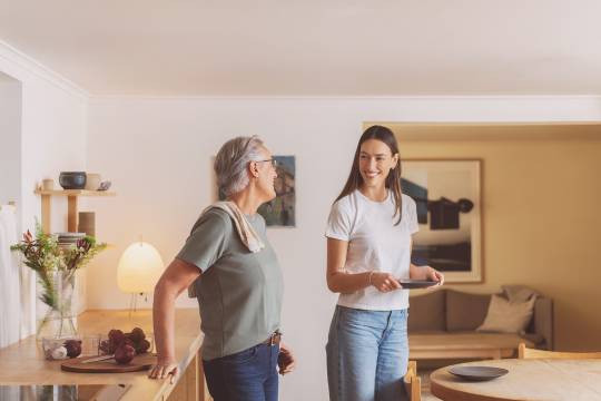 Voksen og ung kvinne smiler og dekker bord på kjøkkenet