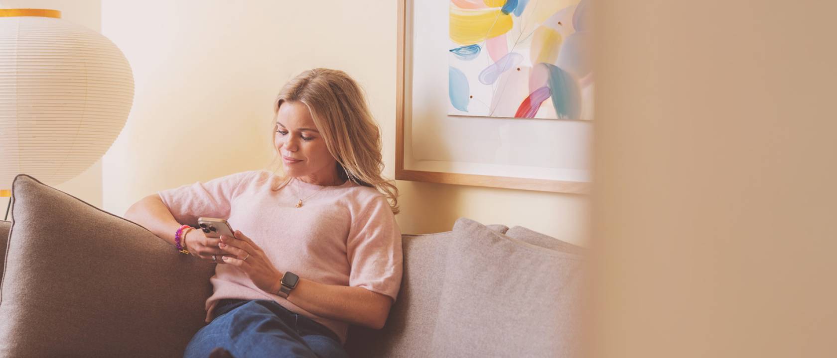 Kvinne i sofa med mobil i hånden
