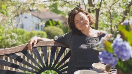 Dame som slapper av på benk i hage på sommeren