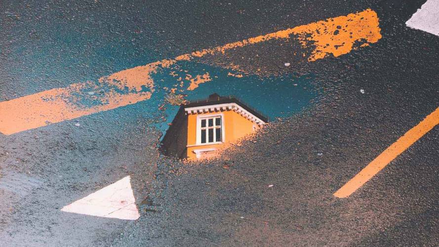 Hus reflektert i vannpytt på veien