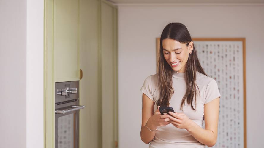 Ung dame med mobil i hendene på kjøkkenet