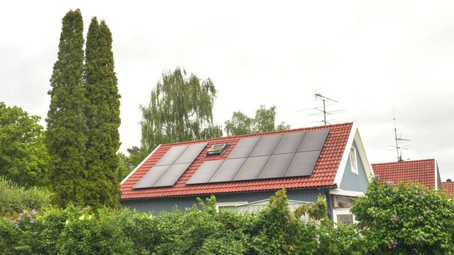 Blågrått hus med solceller på taket omringet av grønne trær og syriner