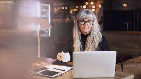 Middelaldrende kvinne sitter ved datamaskin på kafé.
