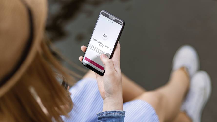 Person med mobiltelefon i høyre hånd, med aktivering av Visa Click to Pay