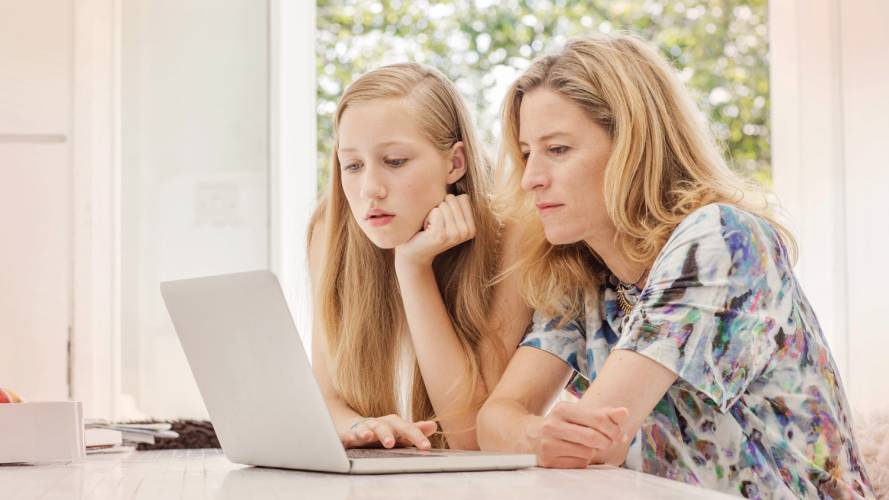 Mor og datter som sitter foran laptop hjemme