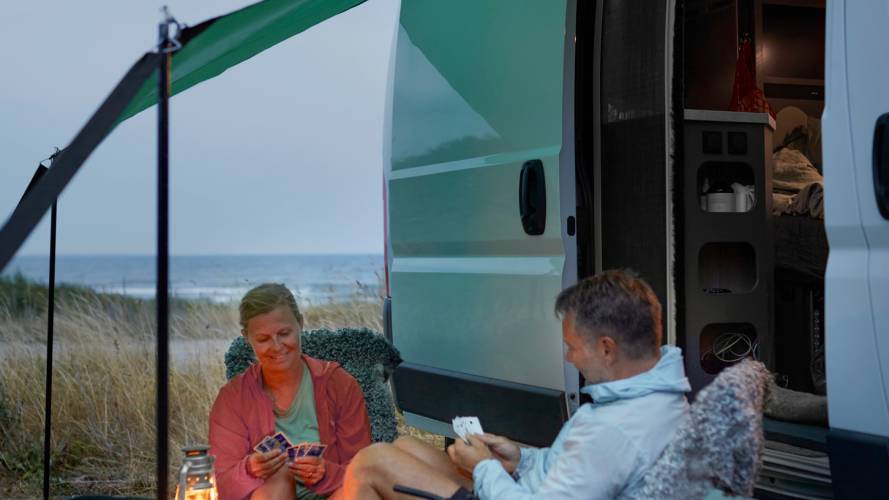 Smilende dame og mann som spiller kort utenfor campingbil på en sommerkveld