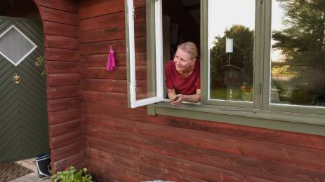kvinna tittar ut av fönster i stuga på landet