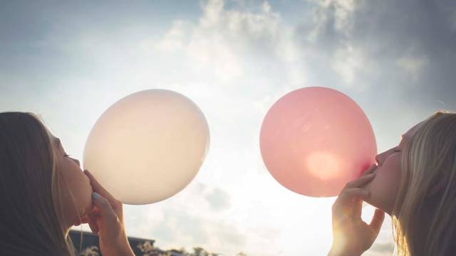 To jenter som blåser ballonger, en hvit og en rosa