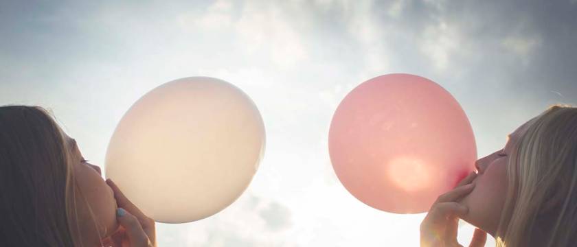 To jenter som blåser ballonger, en hvit og en rosa