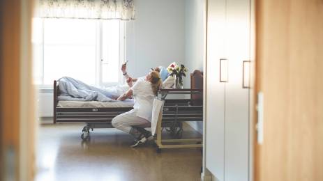 Sykepleier på jobb på sykehus, snakker med pasient i sykesengen