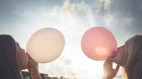 To jenter som blåser ballonger, en hvit og en rosa