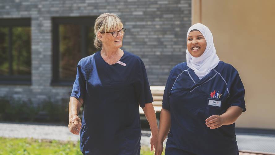 To sykepleiere som går og smiler