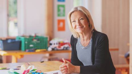 Dame som sitter ved en skolepult og smiler