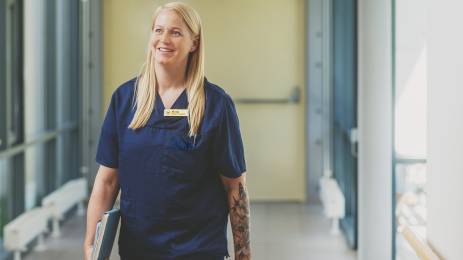 Sykepleier med skrivebok i hånden som går i sykehuskorridor